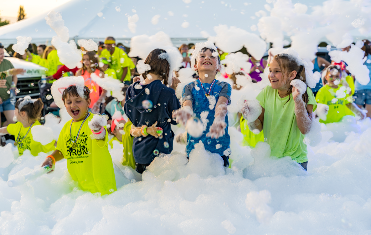 Kids in glow race shirts covered in white foam at an event