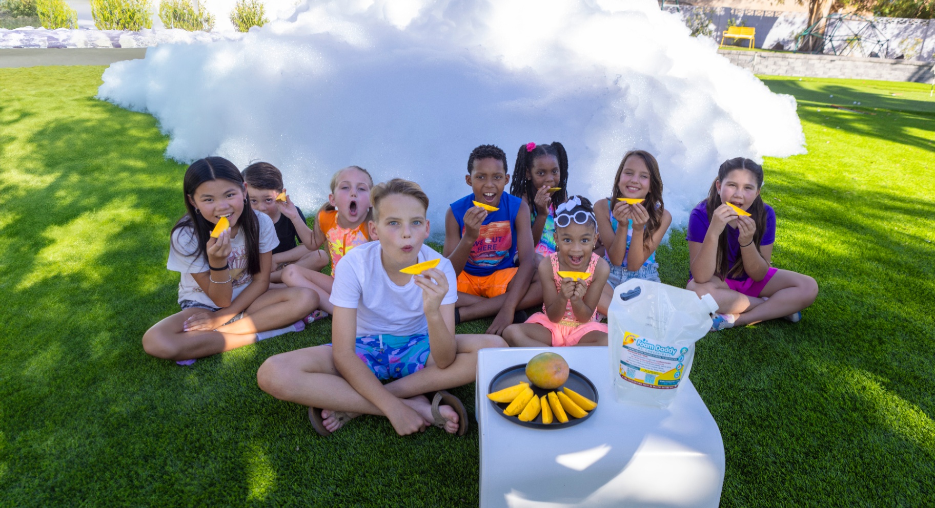 Group of kids eating mango slices in front of a foam cloud