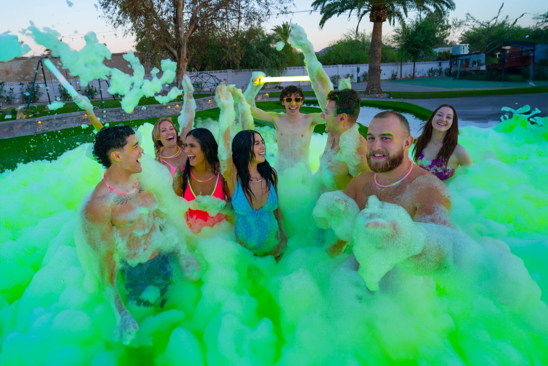 Friends laughing in a pool of green glow foam at sunset