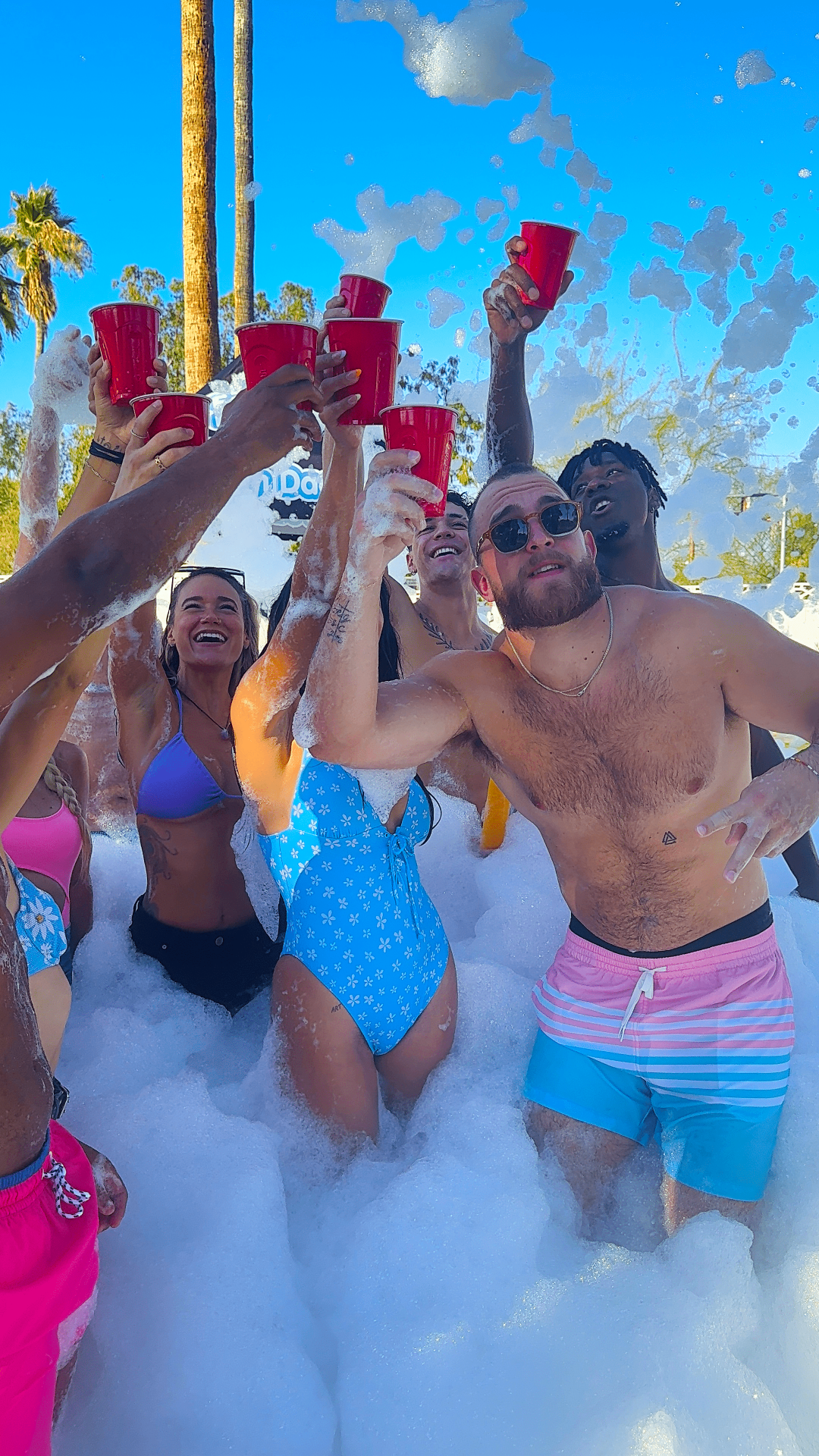 Party guests cheering with red cups in a foam party