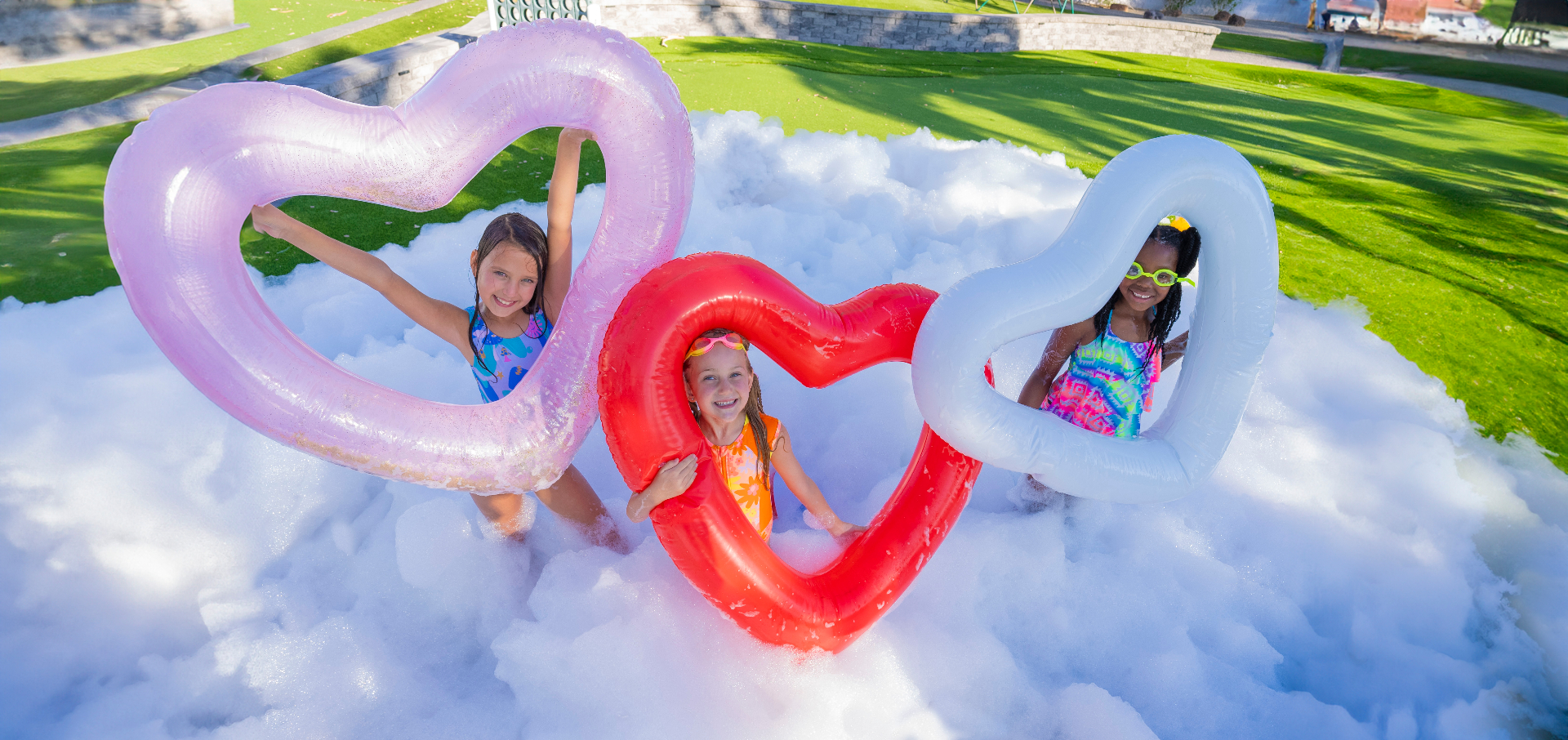 Three girls with heart-shaped floats in a giant foam pit